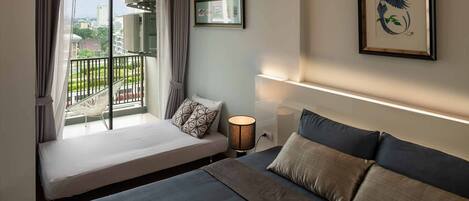 A bedroom with a bed, a bedside table, a lamp, a window with curtains, and a view of the cityscape.