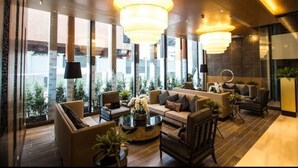Ein stilvoller Lounge-Bereich mit Sofas, Sesseln und einem Couchtisch, großen Fenstern mit Blick auf die Stadt und dekorativer Beleuchtung.