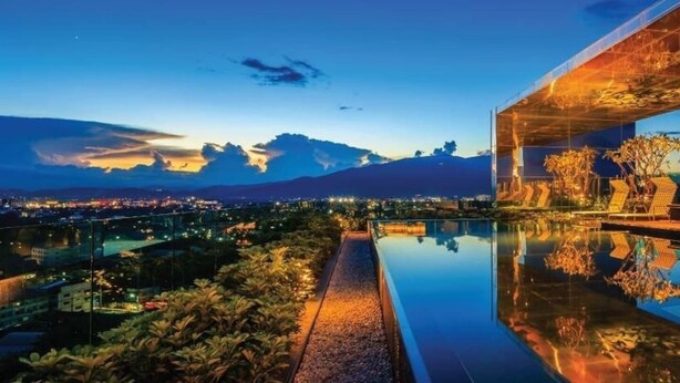 Ein modernes Hotel mit einem spiegelnden Infinity-Pool, Blick auf Berge und Stadtlandschaft im Hintergrund.