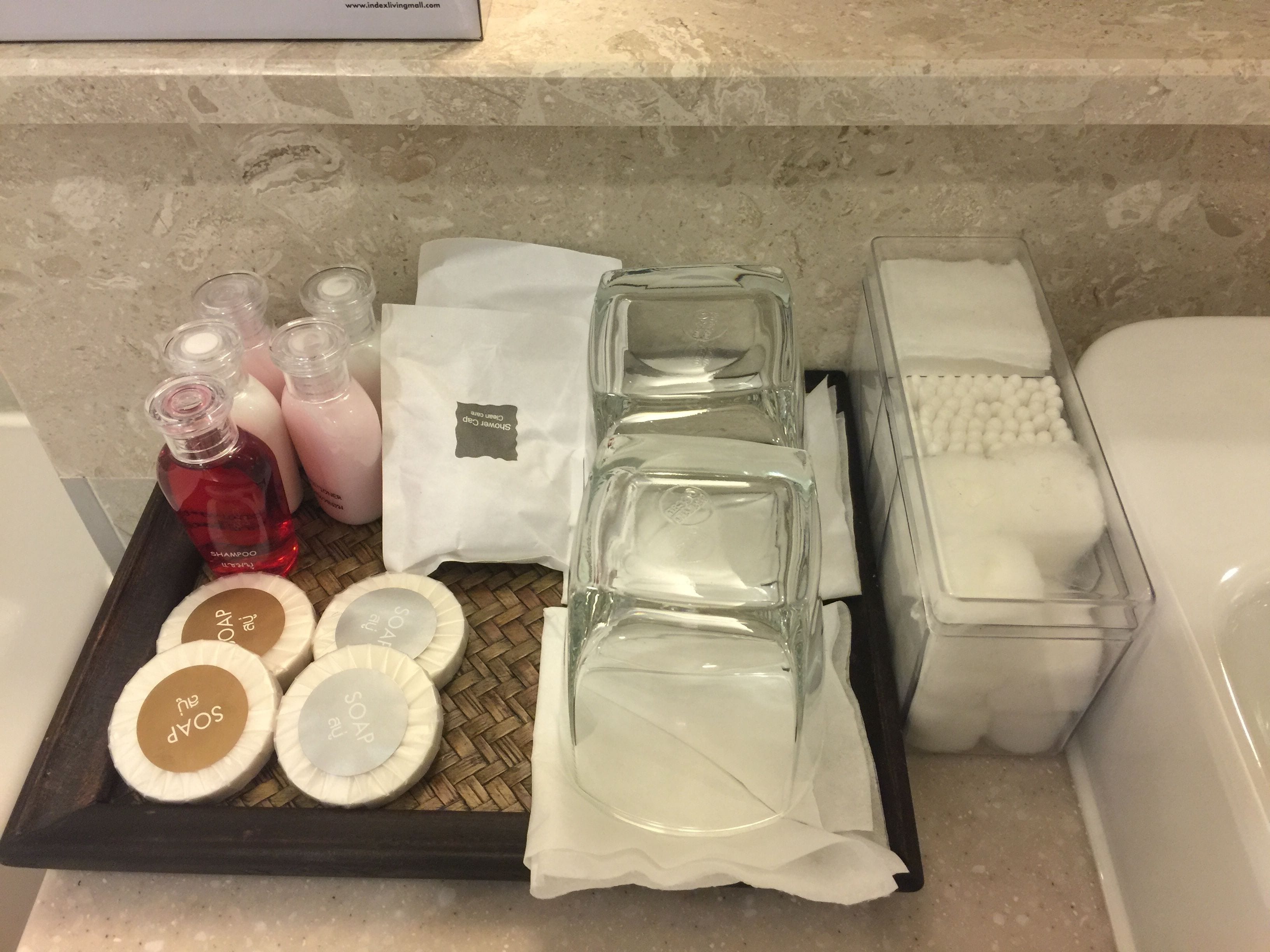 A bathroom vanity with a tray holding various toiletries including bottles of shampoo and soap, a glass jar, and a white towel.