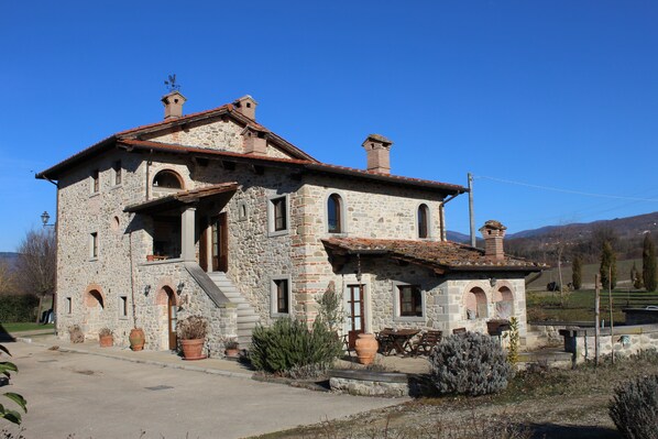 A stone building with a tiled roof, multiple windows, and a staircase leading to the entrance.