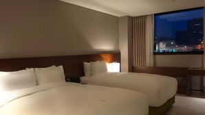 Een hotelkamer met twee grote bedden, een nachtkastje, een lamp en een raam met uitzicht op de stad.