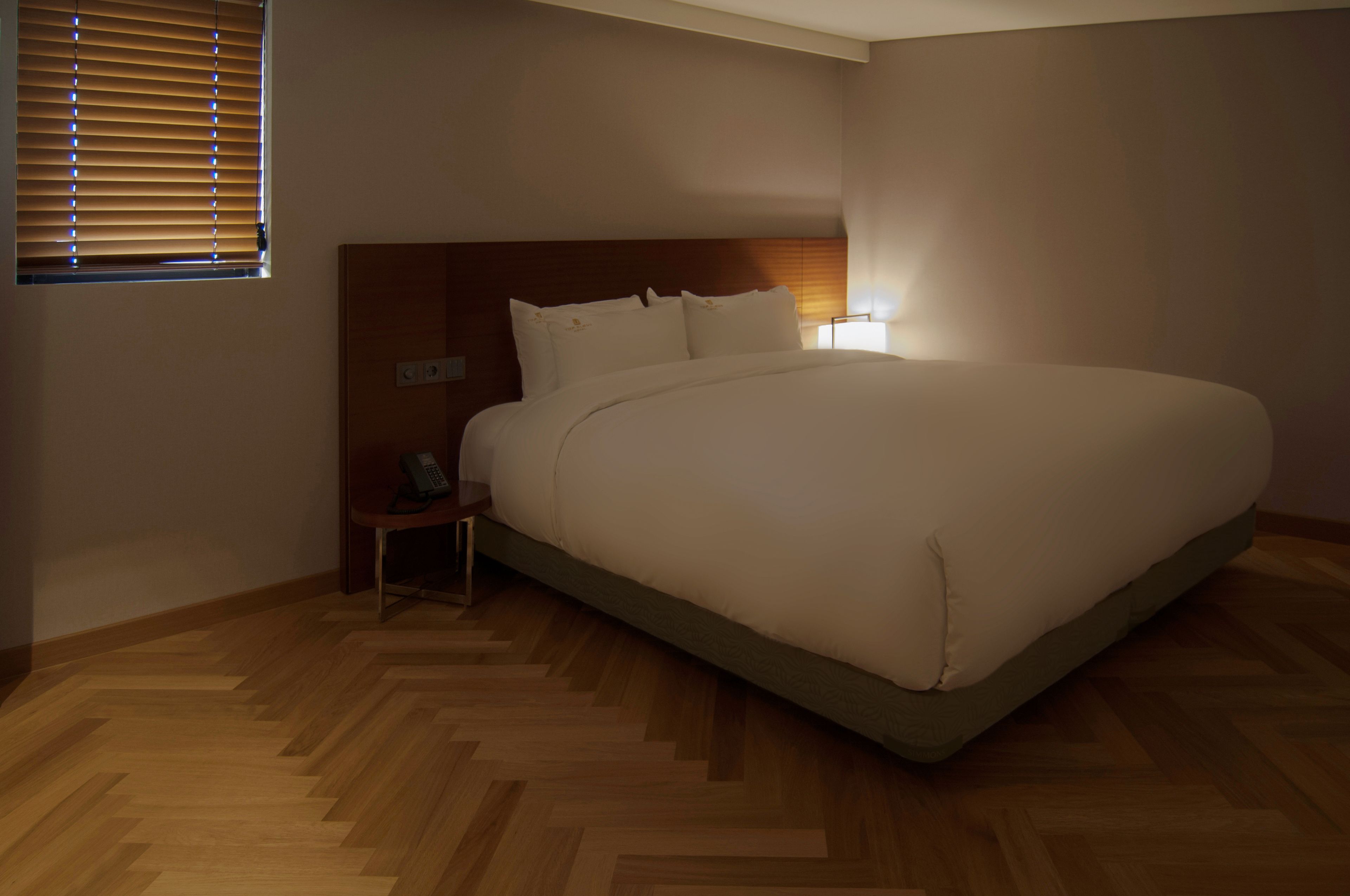 Un dormitorio con una cama grande, un cabecero de madera, una mesita de noche con lámpara y una ventana con persianas.