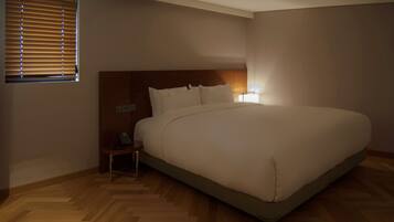 Un dormitorio con una cama grande, un cabecero de madera, una mesita de noche con lámpara y una ventana con persianas.