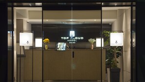 Een receptiebalie met een bord waarop 'Top Cloud Hotel' staat en een scherm dat informatie toont. Aan weerszijden van de balie staan twee potplanten.