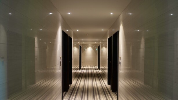 Een moderne hotelgang met een gestreept tapijt, inbouwverlichting en spiegelwanden.