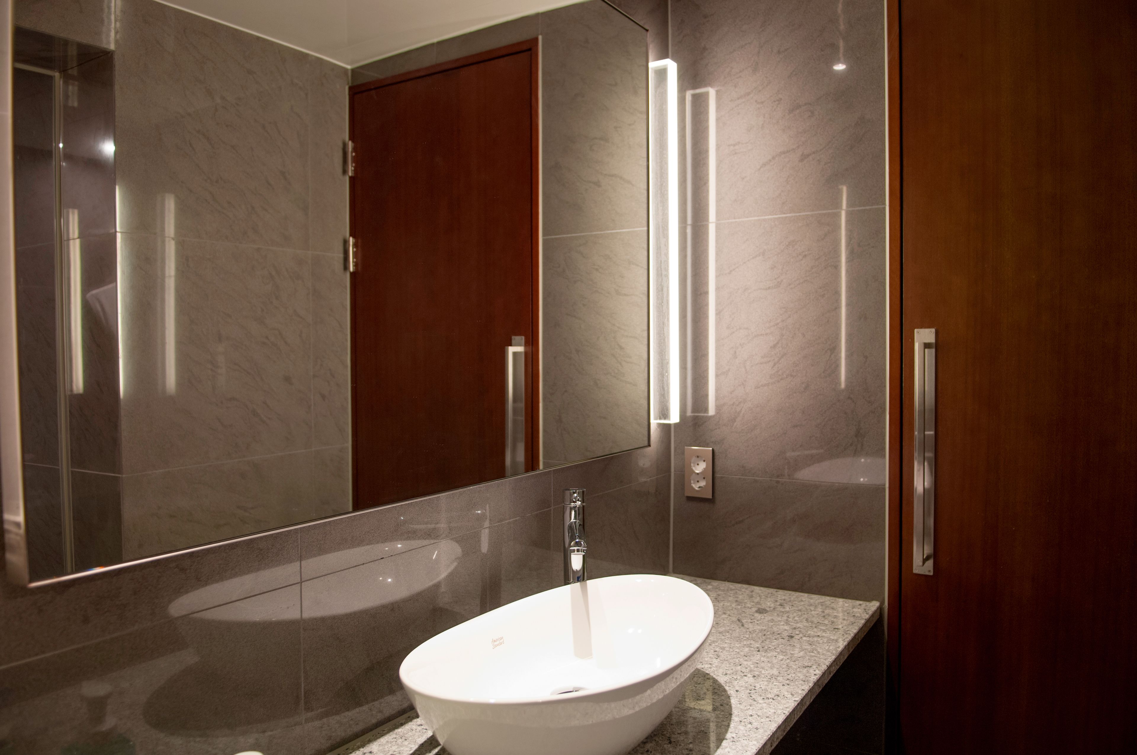 A modern bathroom with a large oval sink, a mirror, and a wooden door.