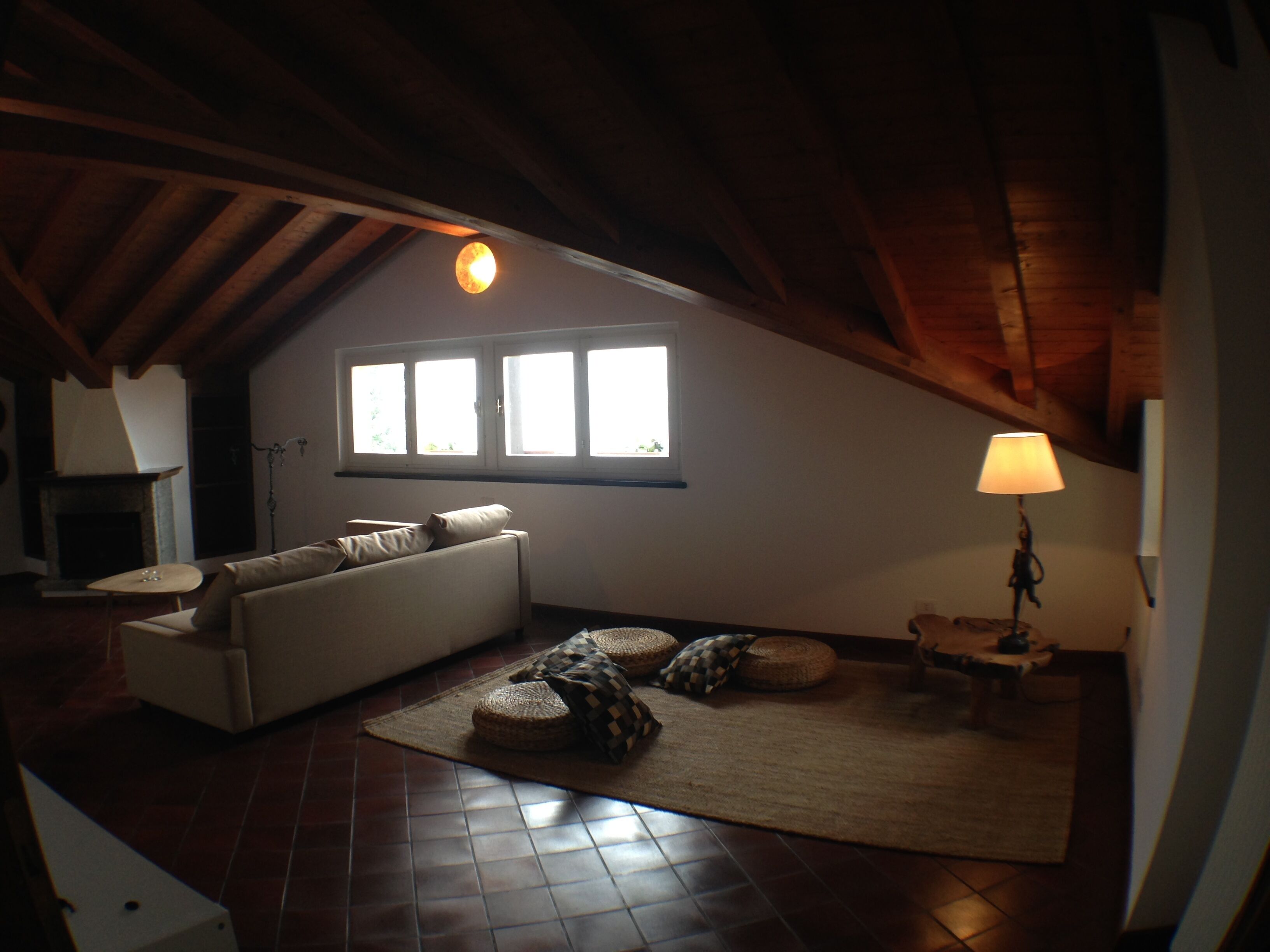 A cozy attic room with a sloped ceiling, a sofa, a lamp, and a view through a window.