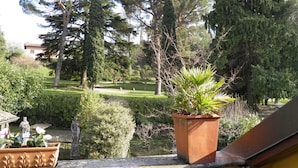A balcony with a potted plant, a stone statue, and a view of a park with trees and a building in the background. - Splendor Luxury Penthouse (cir n. 013250CNI00157) (Bellagio)