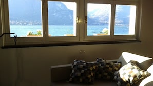 A room with a window overlooking a lake and mountains. There is a white sofa with patterned cushions. - Splendor Luxury Penthouse (cir n. 013250CNI00157) (Bellagio)