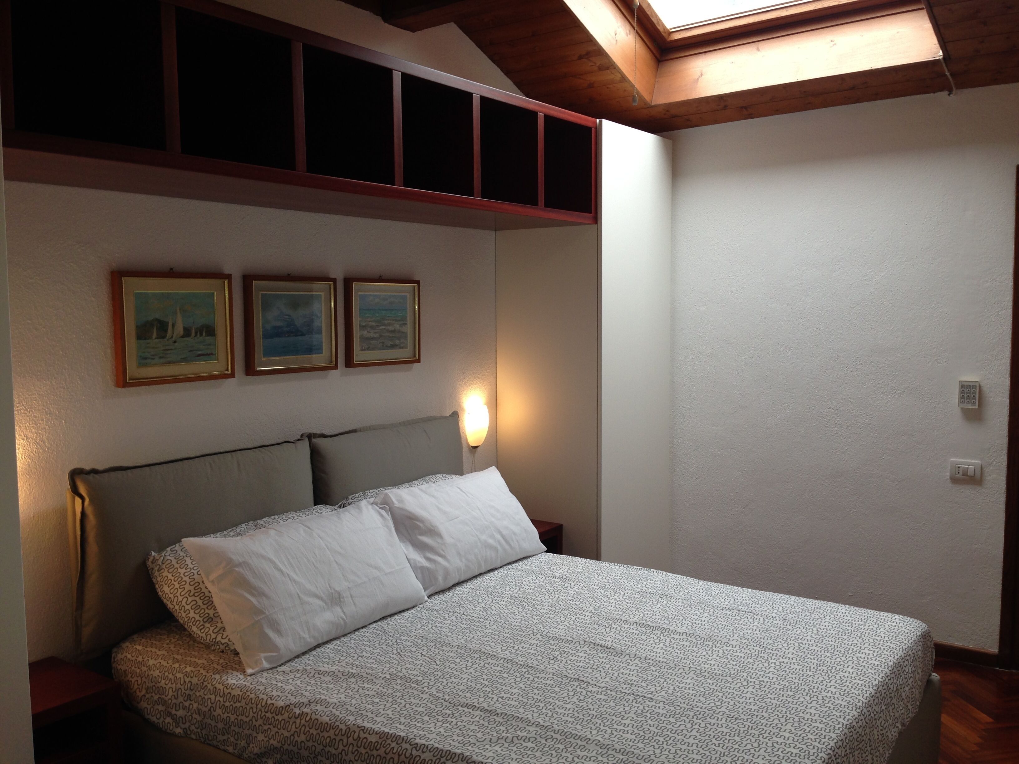 A bedroom with a bed, a nightstand, a wall-mounted light, and three framed pictures.