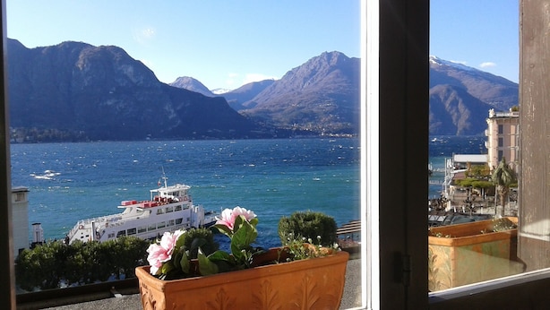 A view of a lake with mountains in the background, a boat, and a building with a balcony. - Splendor Luxury Penthouse (cir n. 013250CNI00157) (Bellagio)