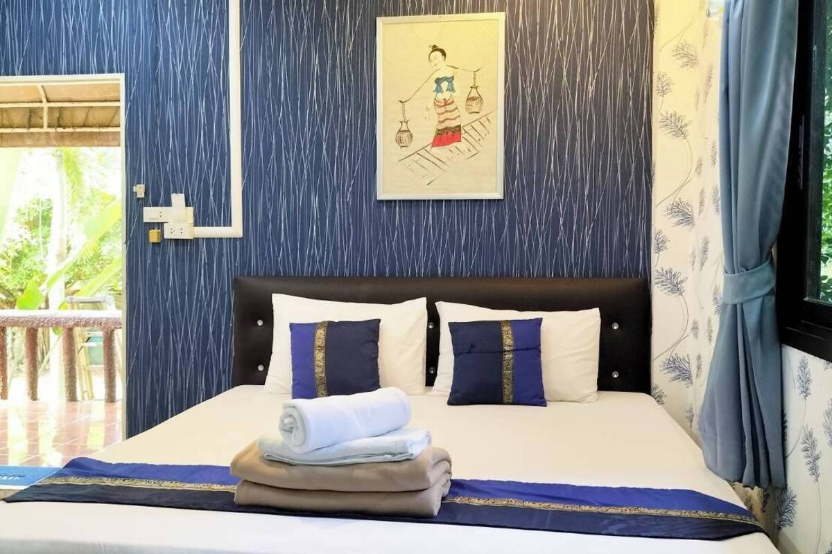 Una cama bien hecha con una colcha azul y blanca, un cojín con diseño azul y dorado, y una toalla doblada sobre la cama.