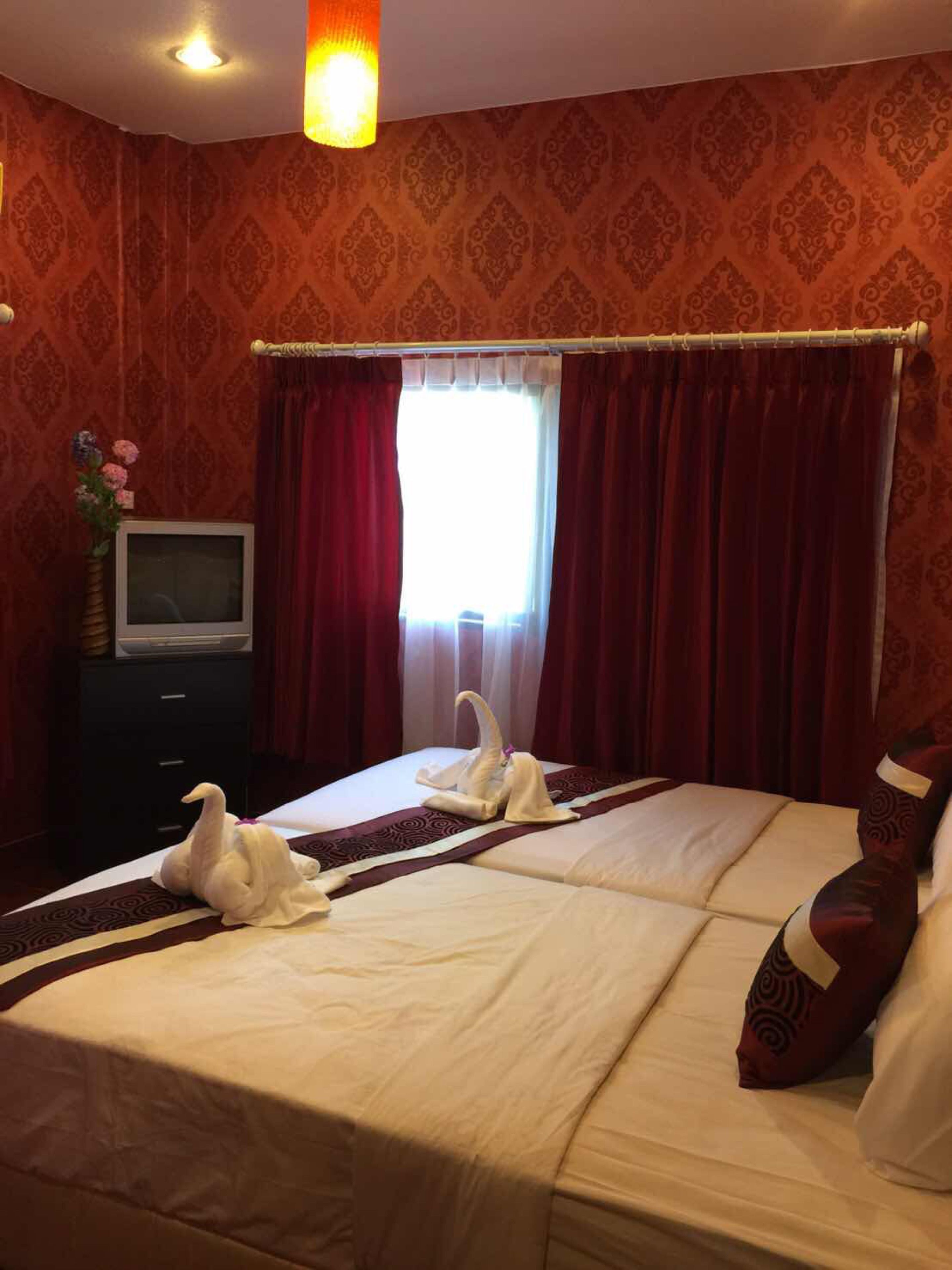 A hotel room with a large bed, red curtains, a TV on a dresser, and a vase with flowers.