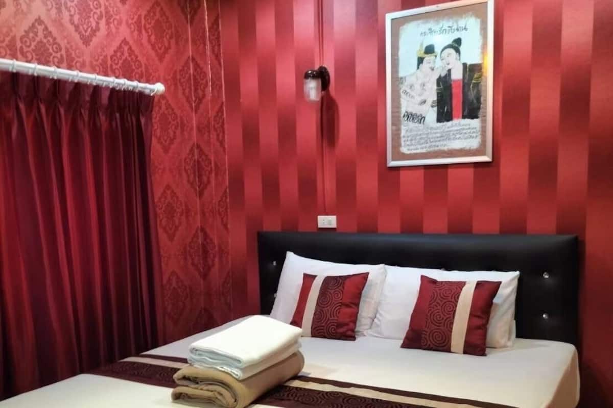 Una habitación de hotel con una cama grande, paredes de color rojo con estampado y un cuadro en la pared.