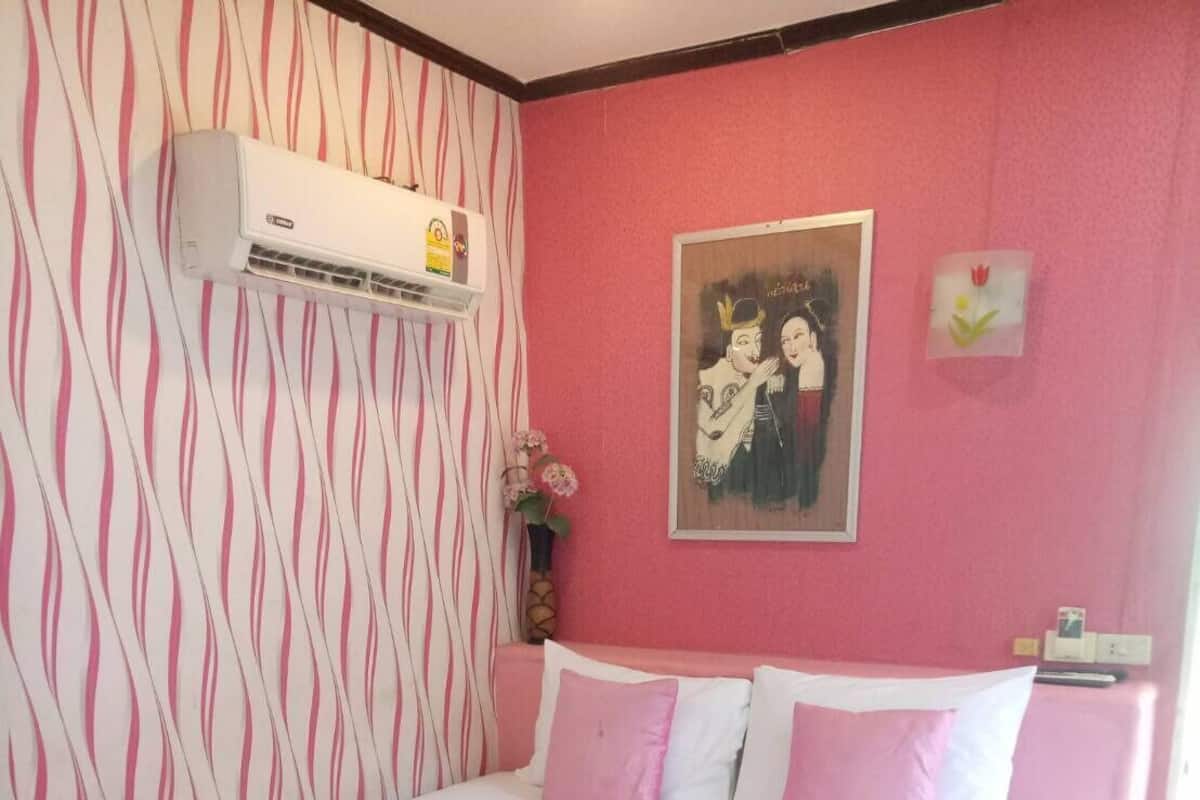 Habitación de hotel con cama, aire acondicionado de pared, un cuadro y un jarrón pequeño con flores.