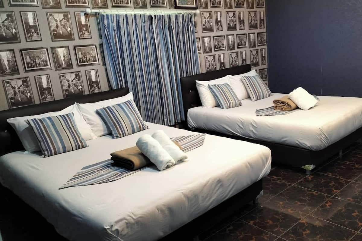 Habitación de hotel con dos camas, cada una con un almohadón a rayas y una toalla doblada. El piso es de baldosas oscuras y la pared está decorada con fotografías en blanco y negro.