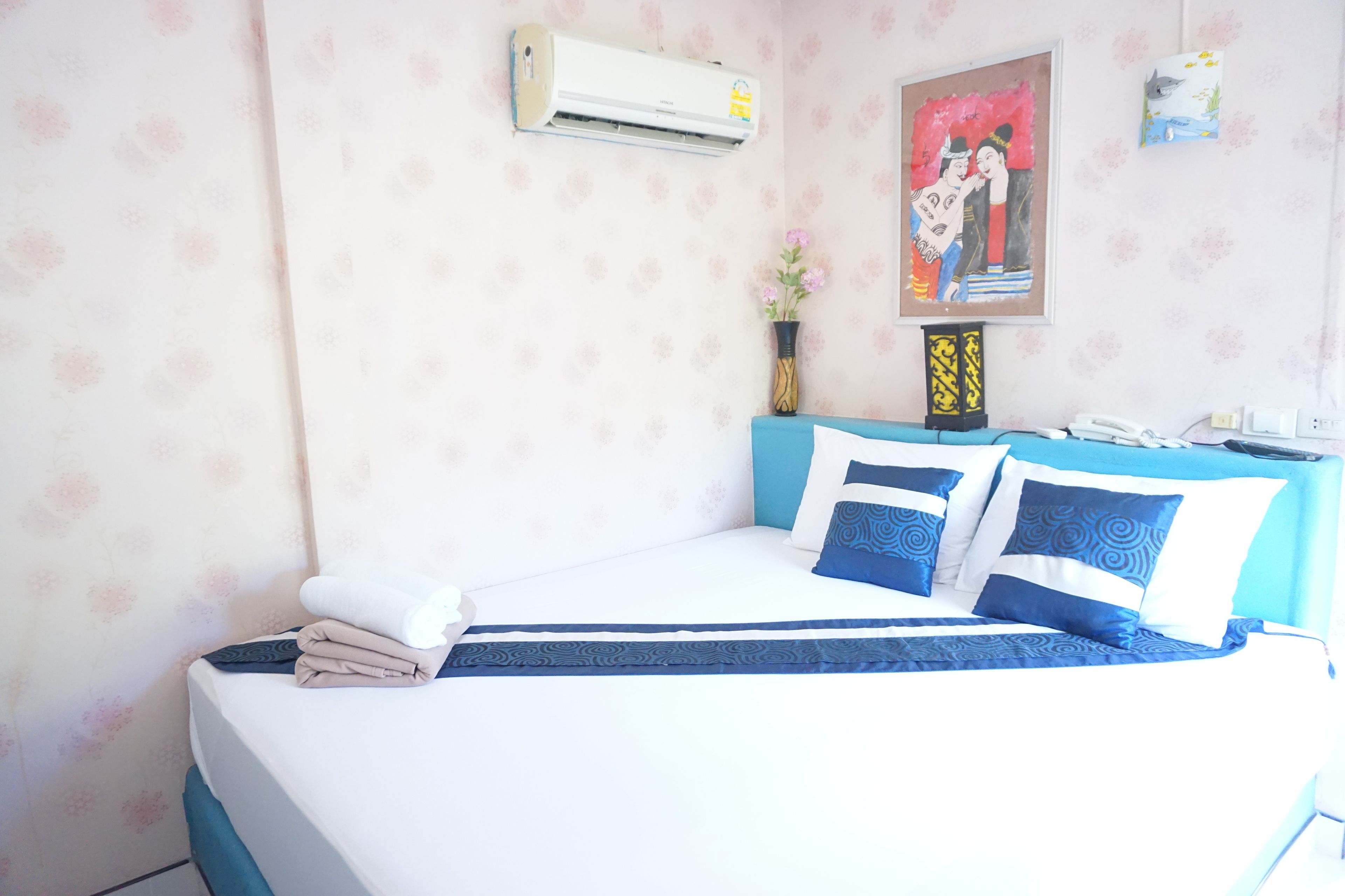 A neatly made bed with blue and white bedding, a wall-mounted air conditioner, and a framed picture on the wall.