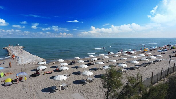 Une plage avec des parasols blancs et des chaises longues, une digue rocheuse et l’océan.