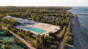 Vue aérienne d’un complexe hôtelier doté d’une grande piscine, d’une plage et d’une zone forestière dense.