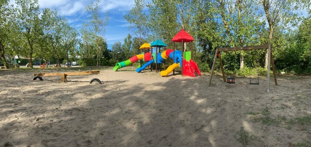 A playground with slides and swings in a sandy area with trees in the background.