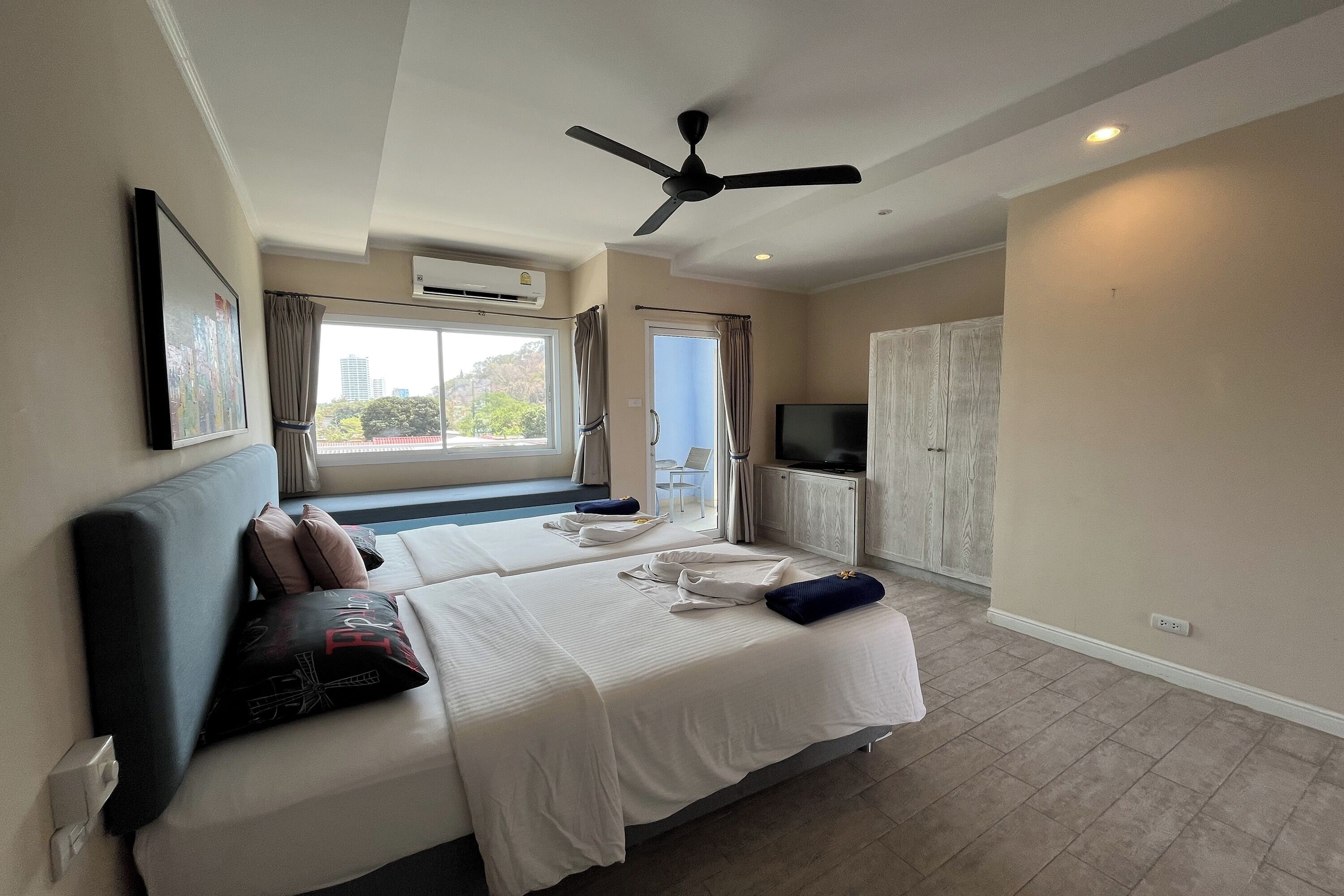 A hotel room with a bed, a ceiling fan, a TV, and a window with curtains.