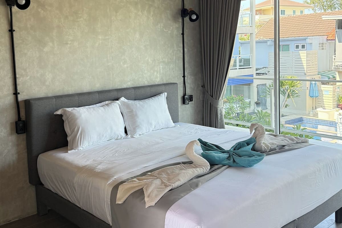 Une chambre d’hôtel moderne avec un grand lit, un ventilateur de plafond et une vue sur les bâtiments environnants.