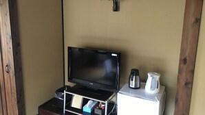 A room with a television on a wooden stand, a white coffee maker, and a small vase with flowers on the wall. - Sujiyu Onsen Daikokuya (Kokonoe)