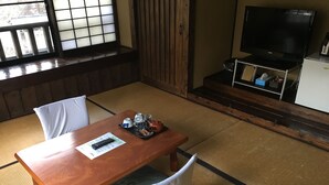 A traditional Japanese-style room with tatami flooring, a wooden table with a remote control and menu, and a television on a stand. - Sujiyu Onsen Daikokuya (Kokonoe)
