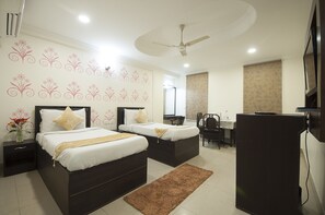 A hotel room with two beds, a desk, a chair, a refrigerator, and decorative wall stickers. - Hotel Dakha International (New Delhi)