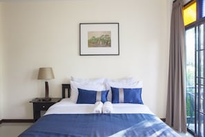 A neatly made bed with blue and white bedding, a framed picture on the wall, and a window with curtains.
