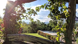 Un banco de madera en un jardín con piscina y montañas al fondo.