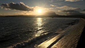 A beach with a curved shoreline, calm water, and a sunset in the background.