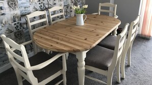A dining area with a wooden table and white chairs, a white pitcher with flowers, and a nautical-themed wall.
