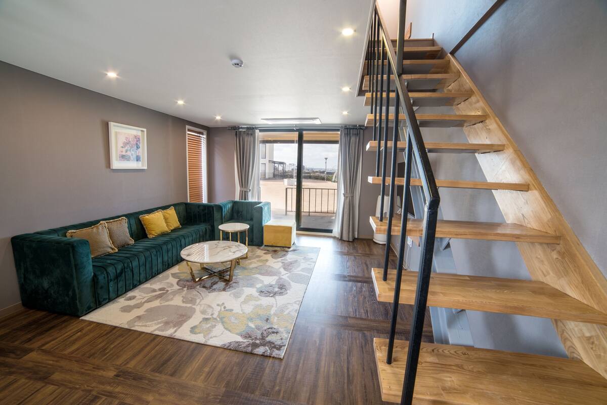 Ein modernes Wohnzimmer mit einem grünen Sofa, einem runden Couchtisch und einer Holztreppe.