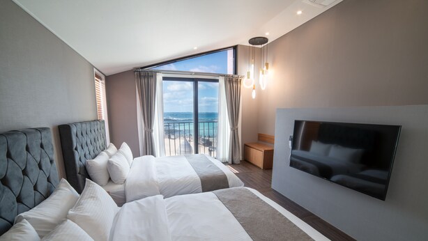 A hotel room with two beds, a TV, and a balcony with a view of the sea.
