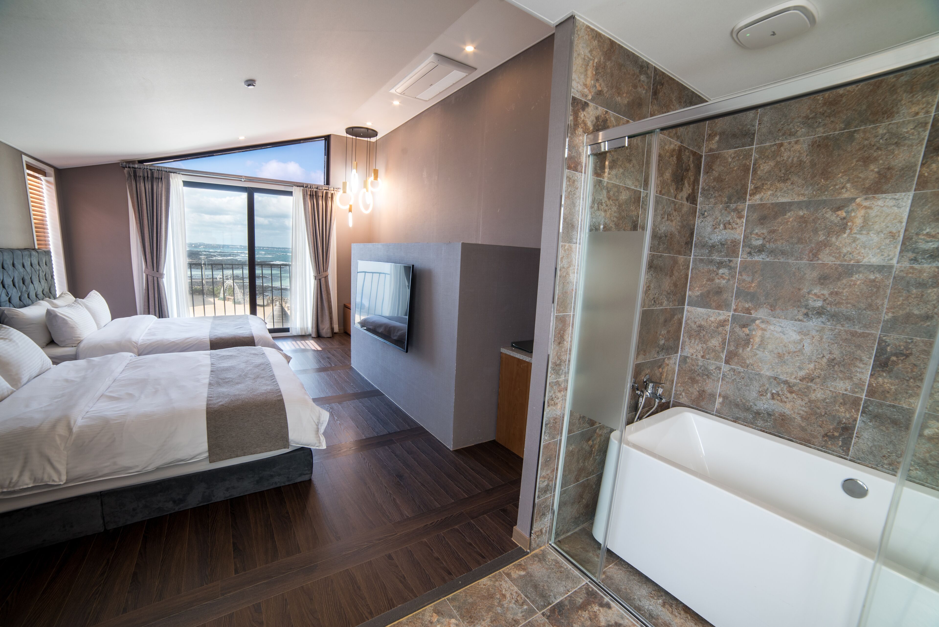 A modern hotel room with a large bed, a separate shower area, and a view of the city.