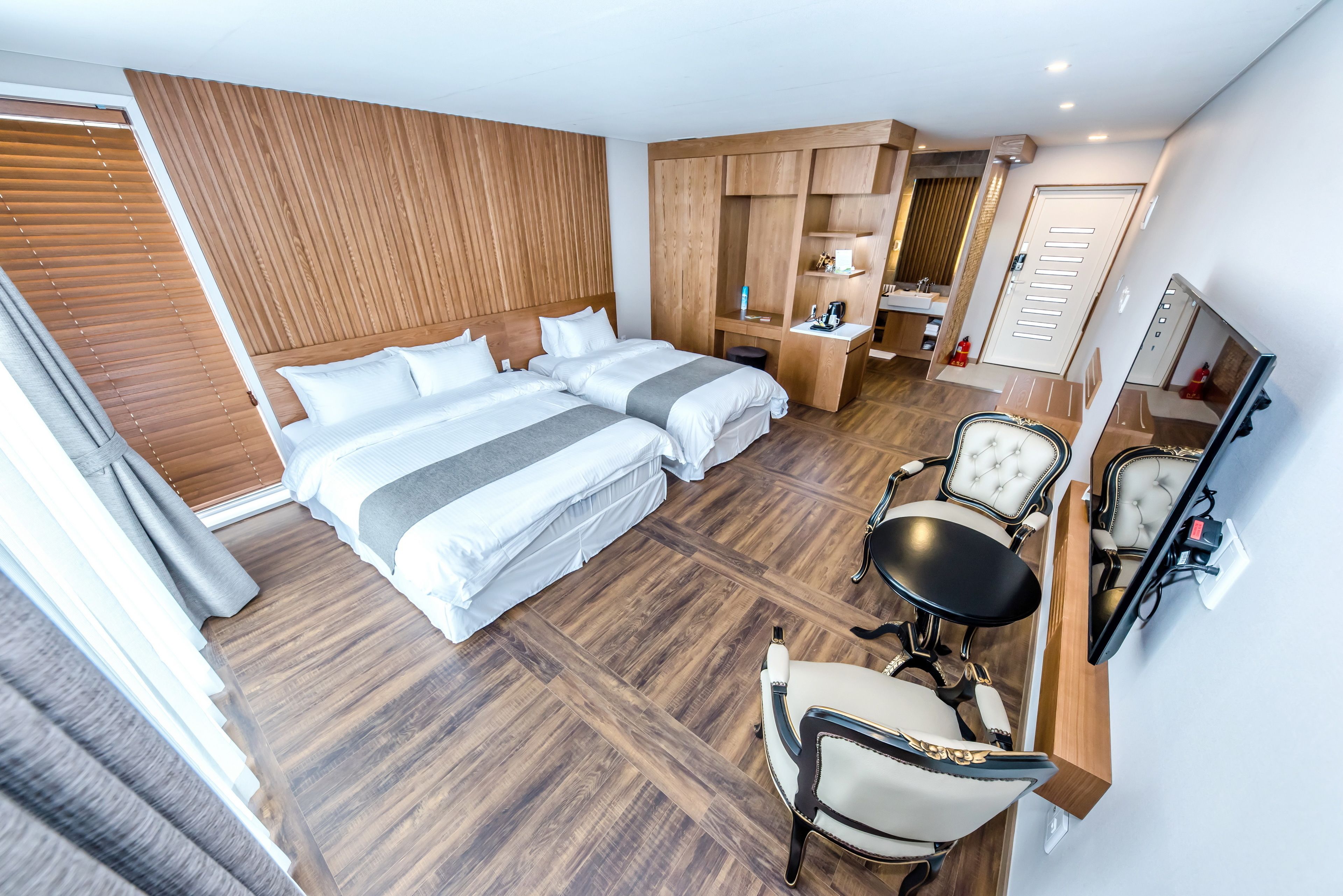 A modern hotel room with a large bed, a desk, a chair, and a mirror.