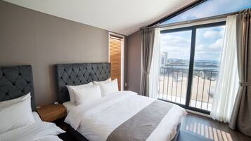 A modern hotel room with a large bed, a nightstand, and a view of the city through large windows.