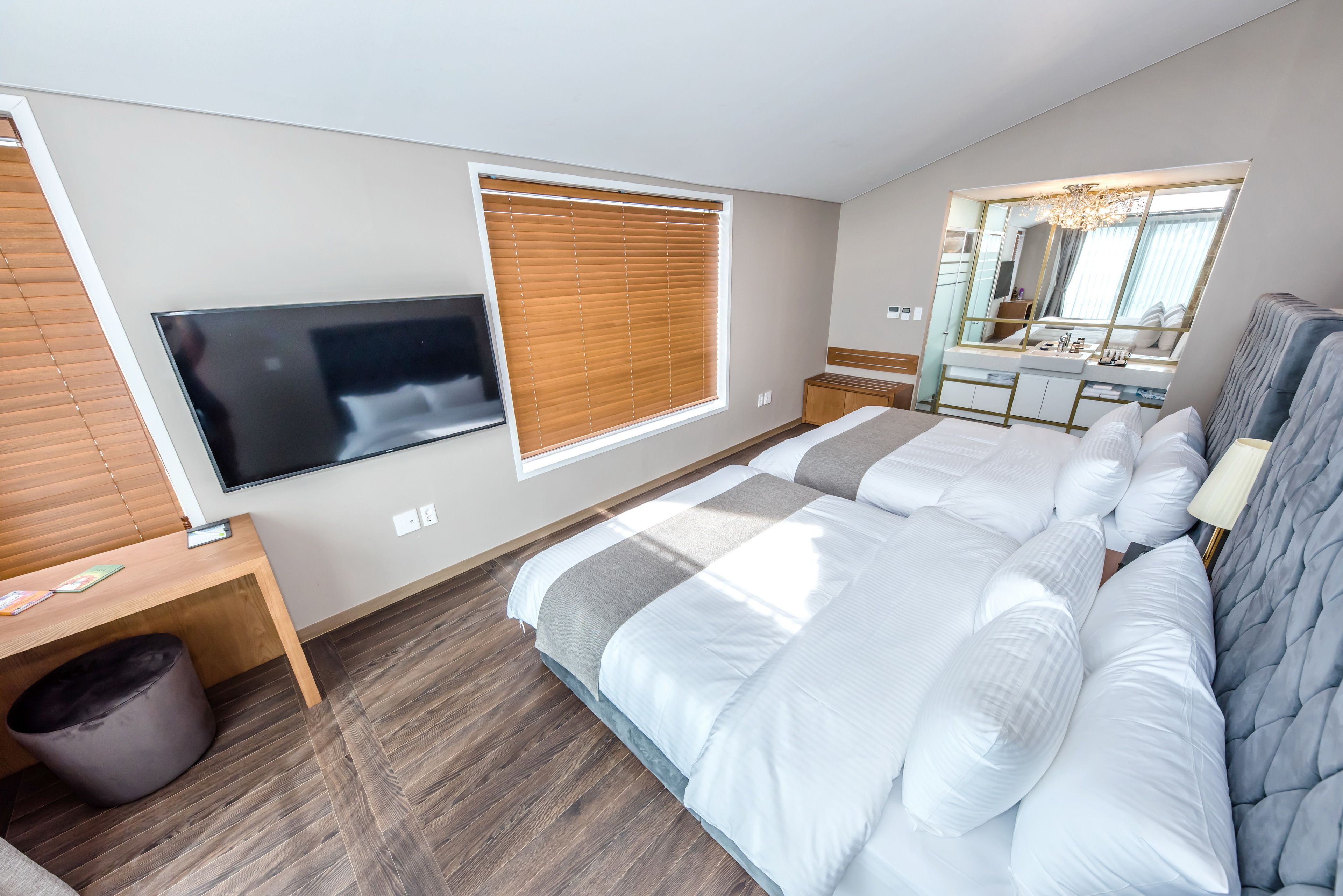 Quarto moderno com uma cama grande, televisão montada na parede, janela com persianas, toucador com espelho e lixeira.