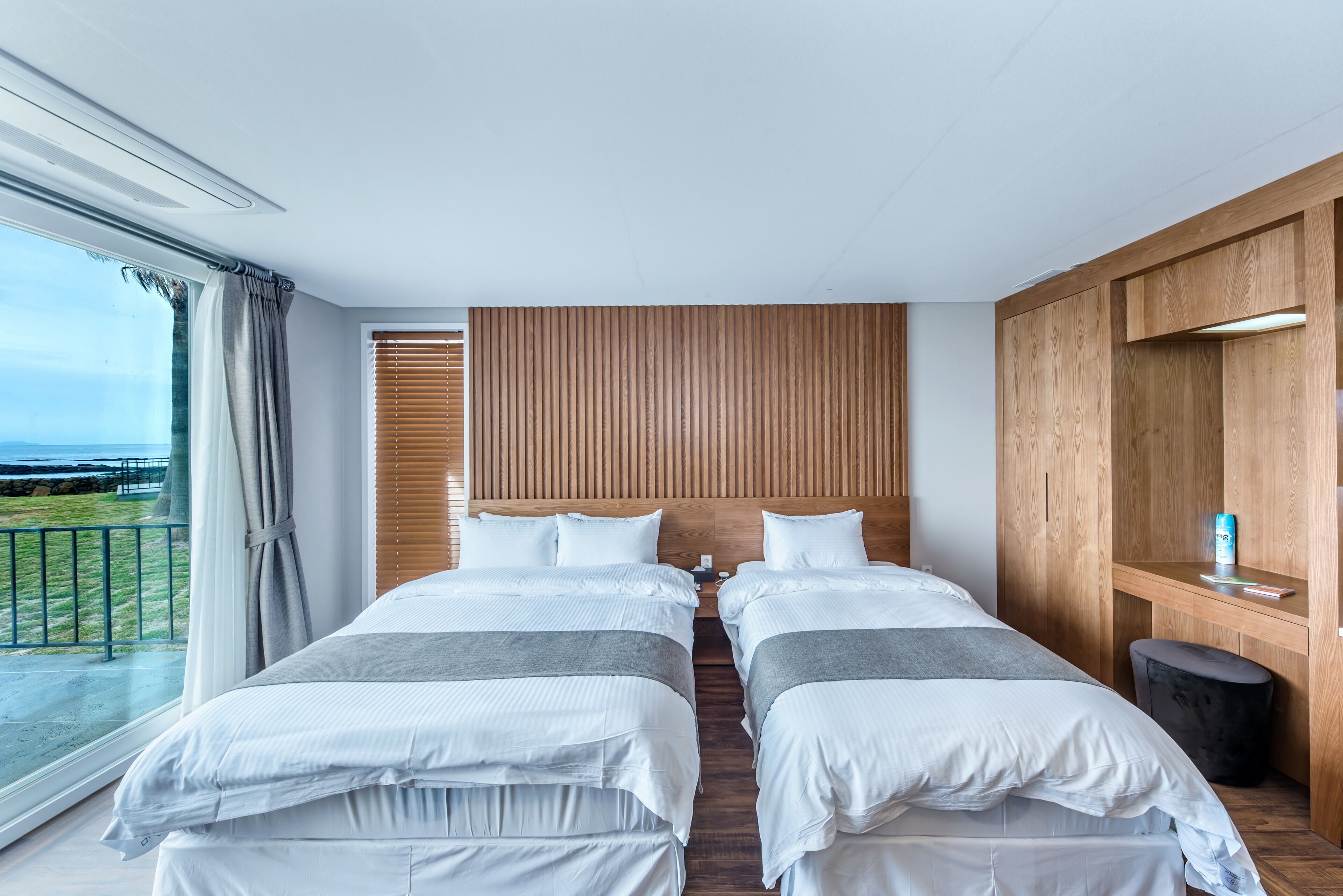 Habitación de hotel con dos camas, un cabecero de madera, un ventanal con cortinas y vistas al exterior.