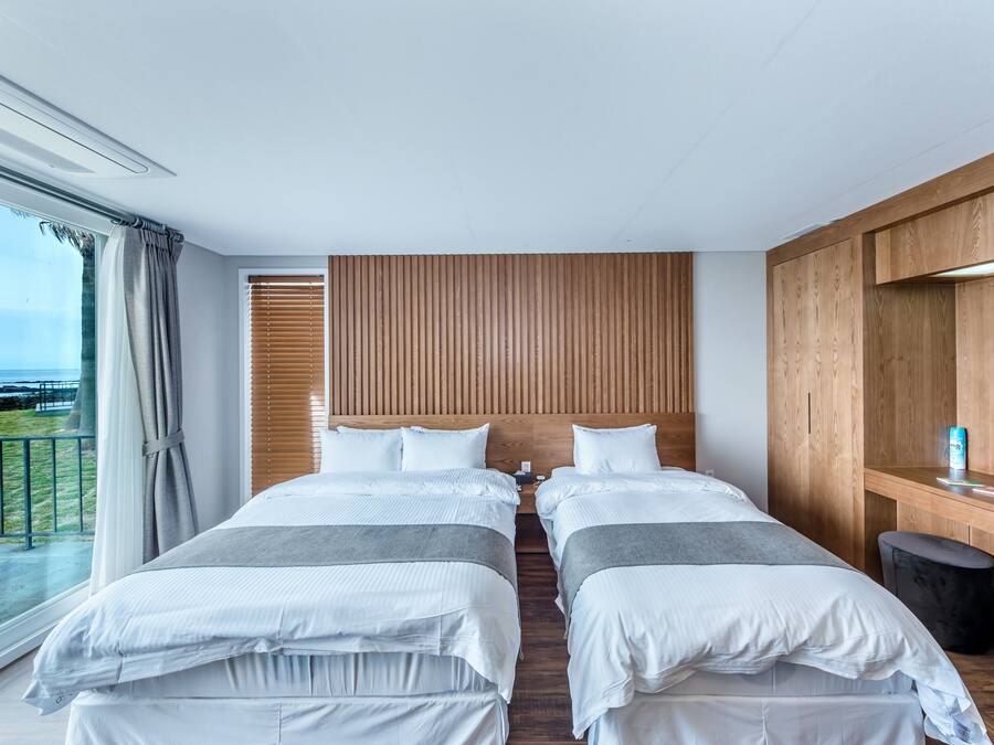 Habitación de hotel con dos camas, un cabecero de madera, un ventanal con cortinas y vistas al exterior.