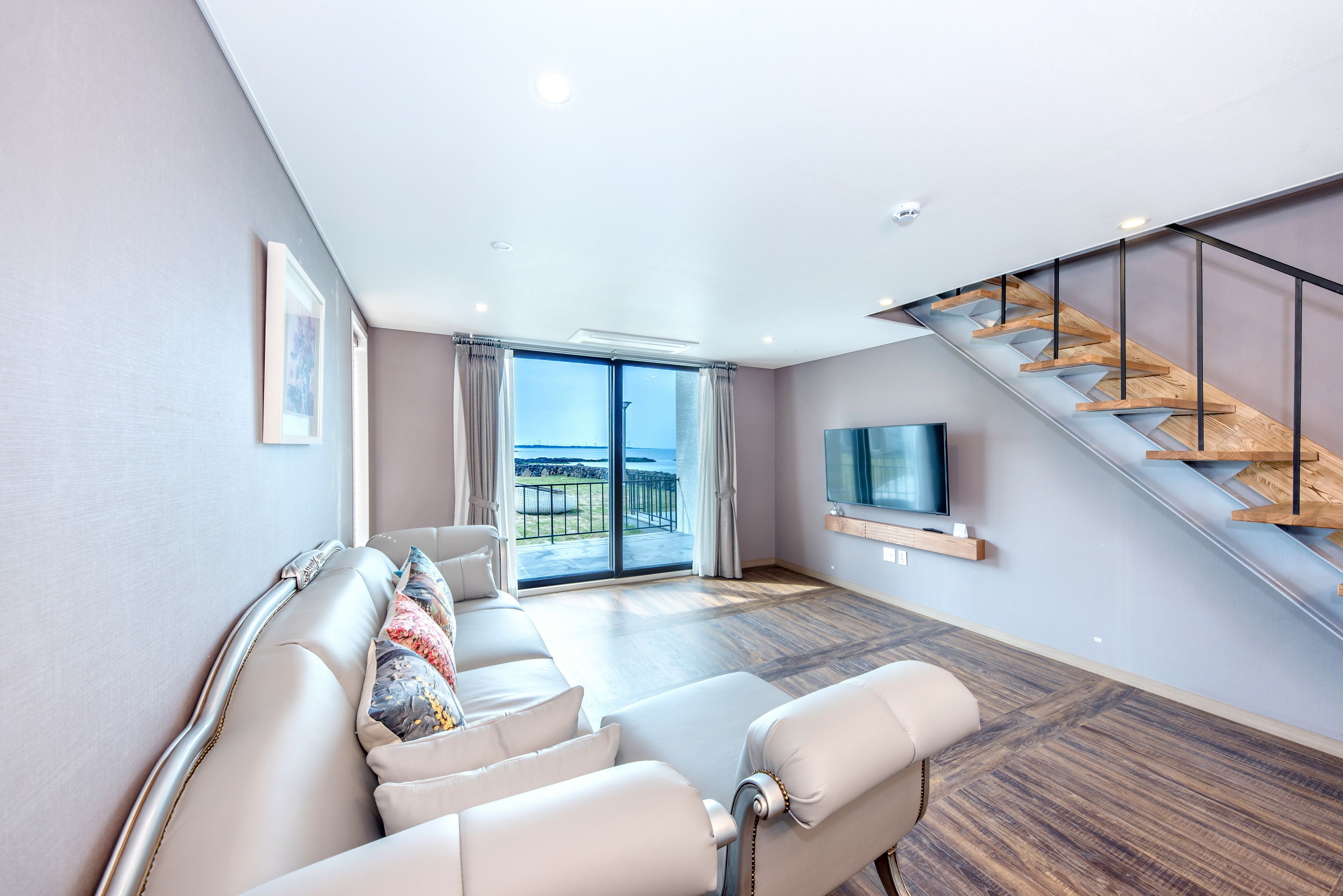 A modern living room with a sofa, a TV, and a staircase.