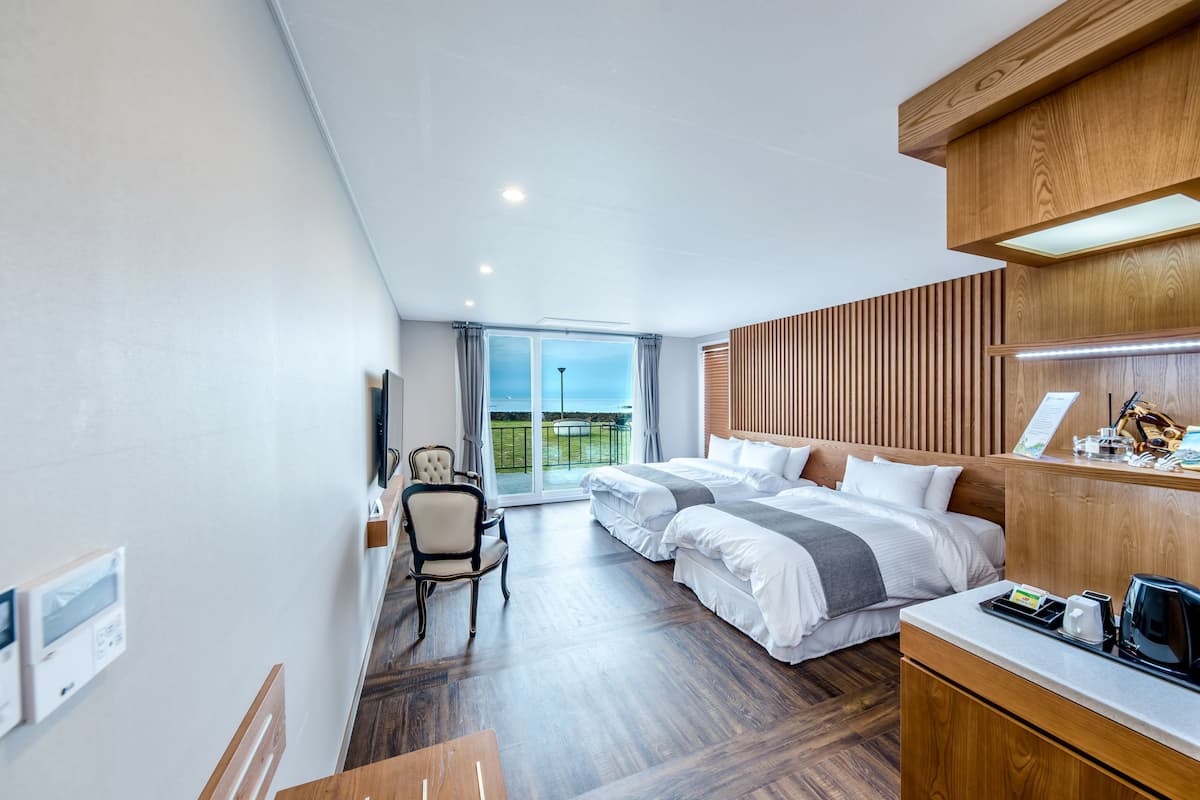 Ein modernes Hotelzimmer mit einem großen Bett, einem Schreibtisch, einem Sessel und Blick ins Freie.