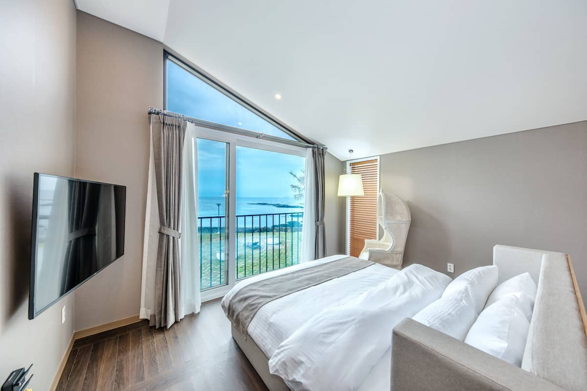 Ein modernes Hotelzimmer mit einem großen Bett, einem Flachbildfernseher, einem Balkon mit Meerblick und einer Lampe.