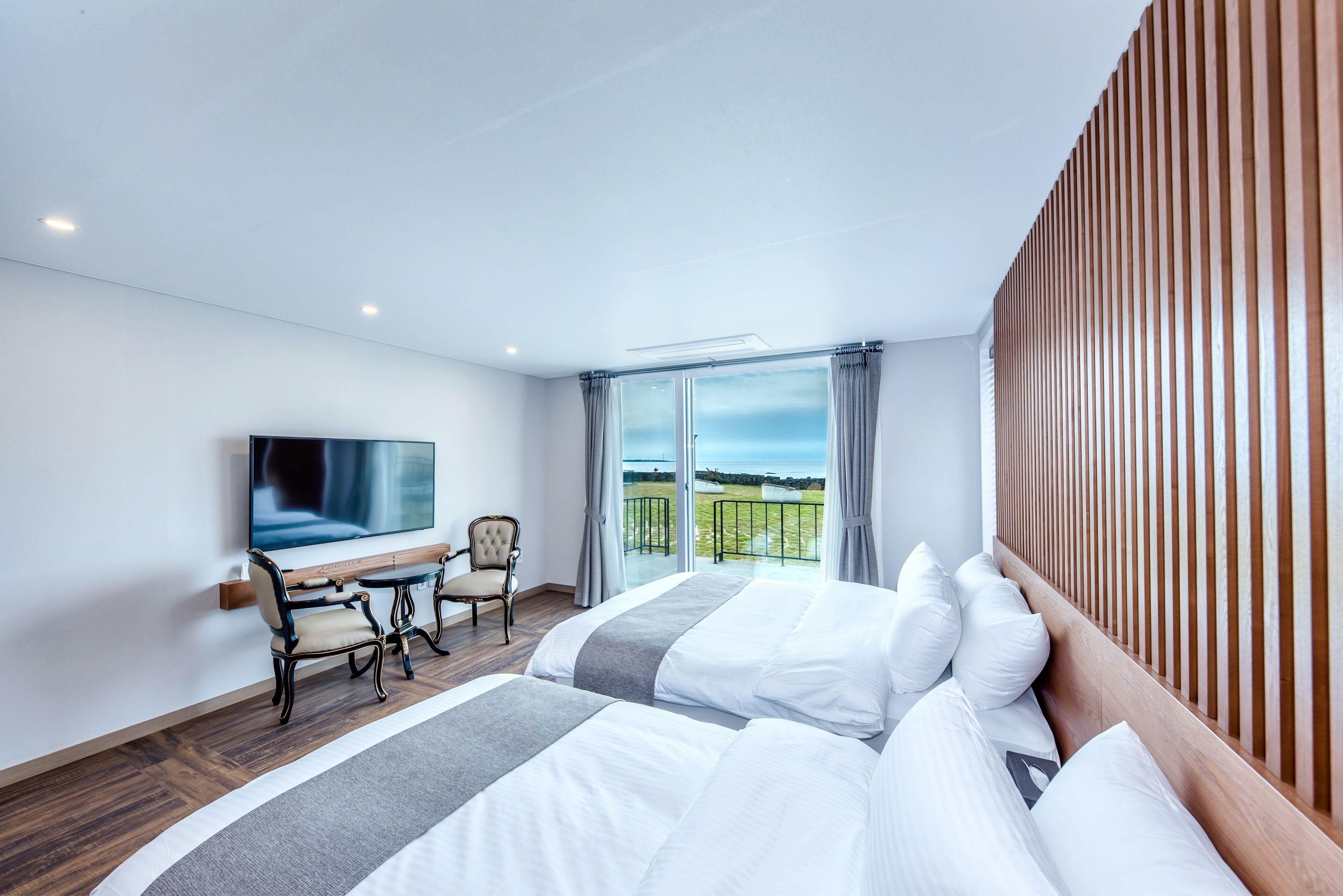 A hotel room with a large bed, a TV, a desk with chairs, and a balcony with a view.
