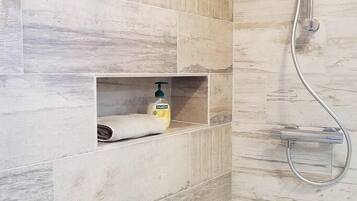 Een badkamer met een douche, een handdoek en een zeepdispenser op een plank.