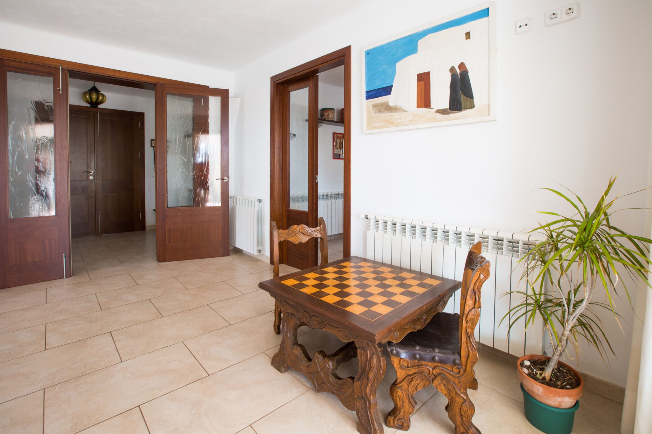 A dining area with a wooden table and chairs, a potted plant, and a painting on the wall.