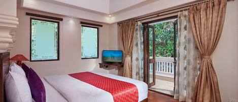 Une chambre d’hôtel avec un lit, une télévision, un balcon avec des rideaux et une vue sur la verdure.