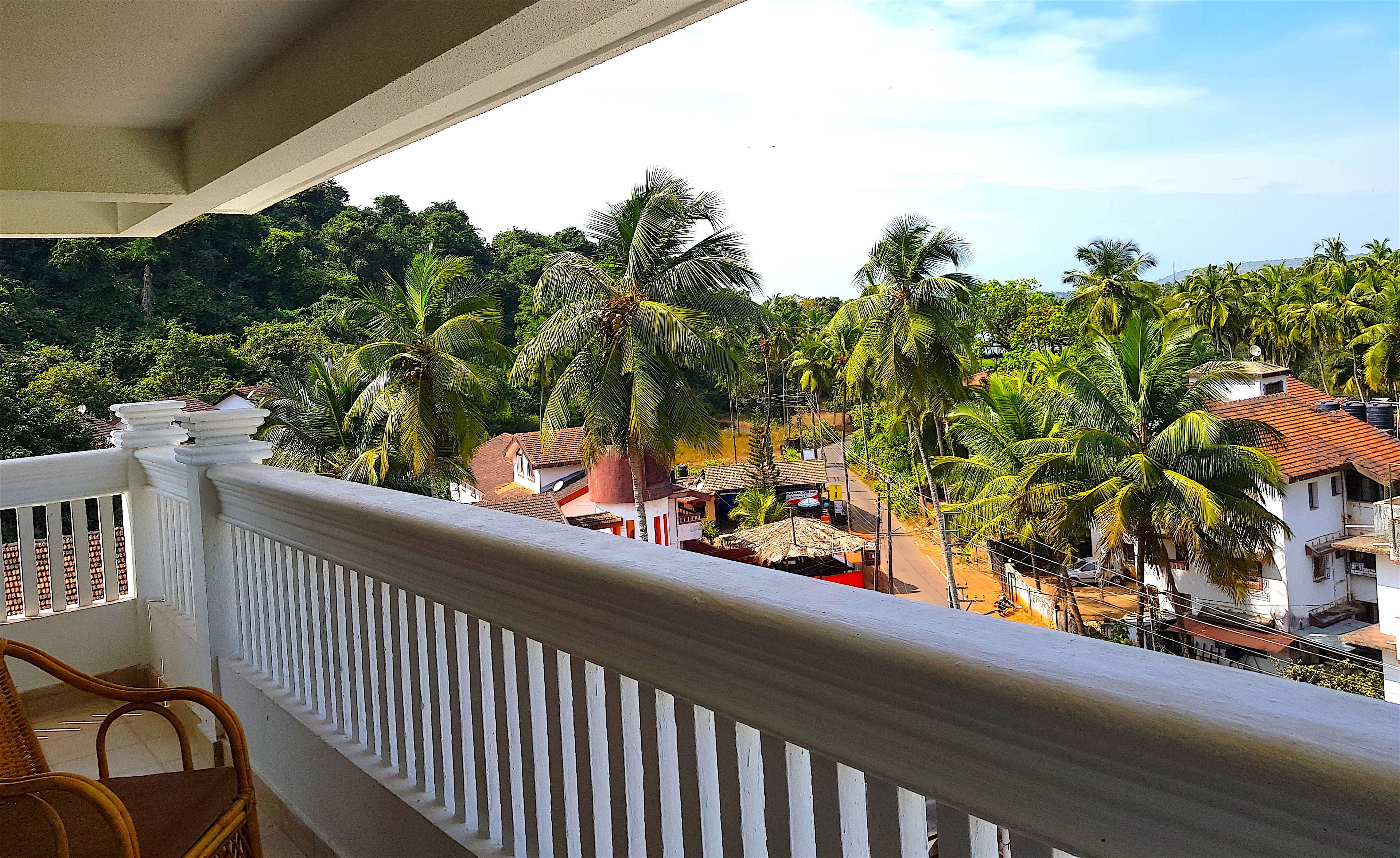 A balcony with a white balustrade overlooking a residential area with palm trees and houses.